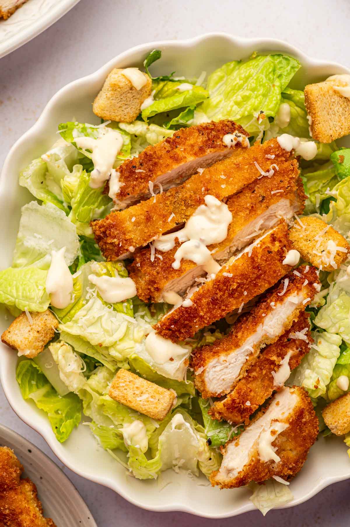 CLose up shot of crispy chicken caesar salad in a white bowl drizzled with salad dressing.