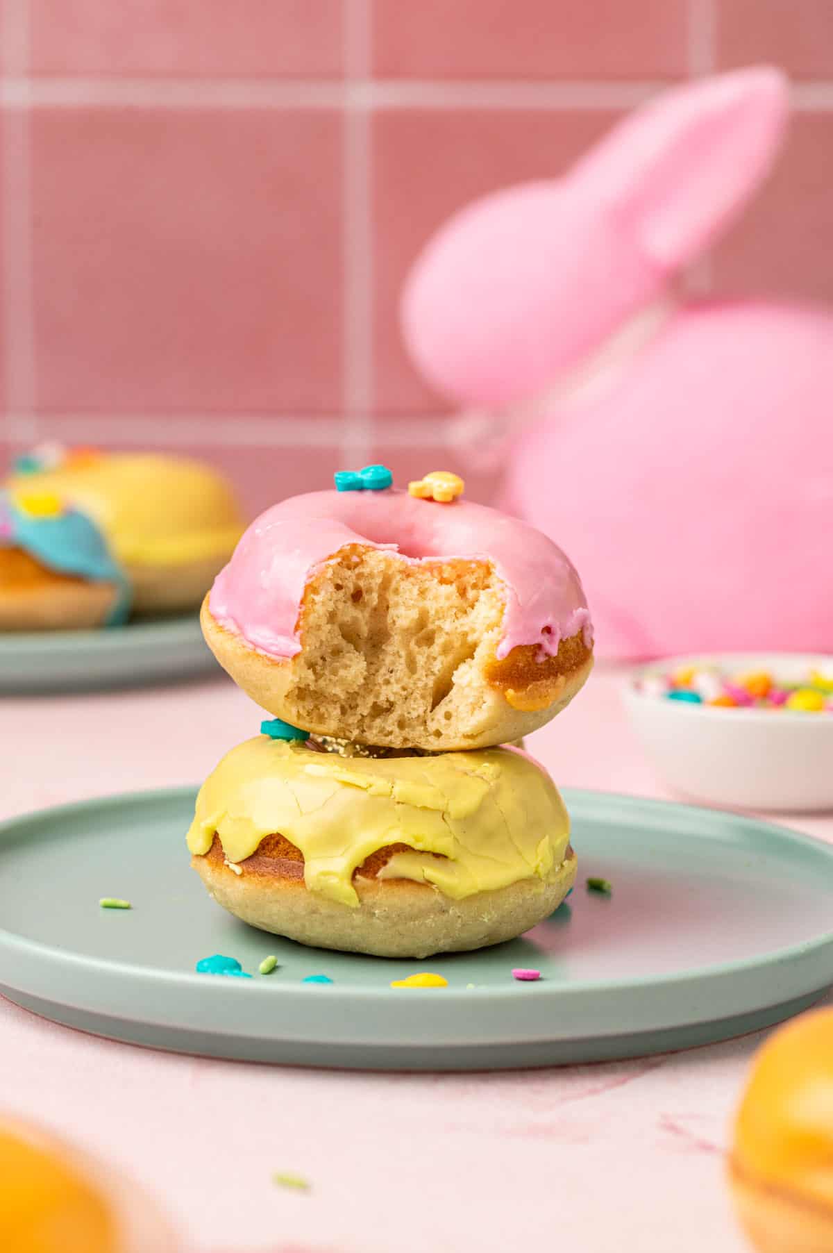 Showing the inner texture of the beautifully decorated Easter donuts stacked one above the another on a blue plate in pink background.