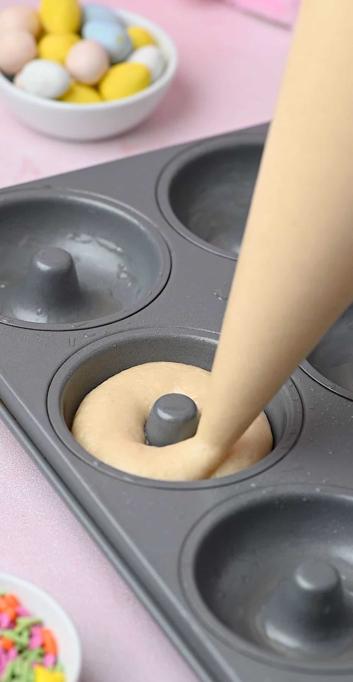 Donut pan cavity being filled with the batter using a piping bag.