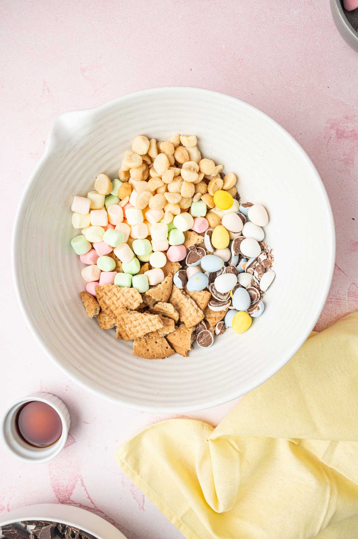 Mini eggs, mini marshmallows, nut, biscuits in a white bowl to make Easter rocky road recipe.