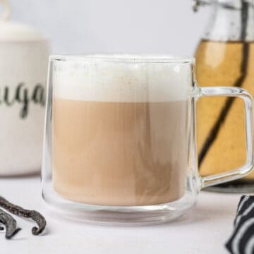 Horizontal image homemade vanilla bean latte in a clear glass mug.