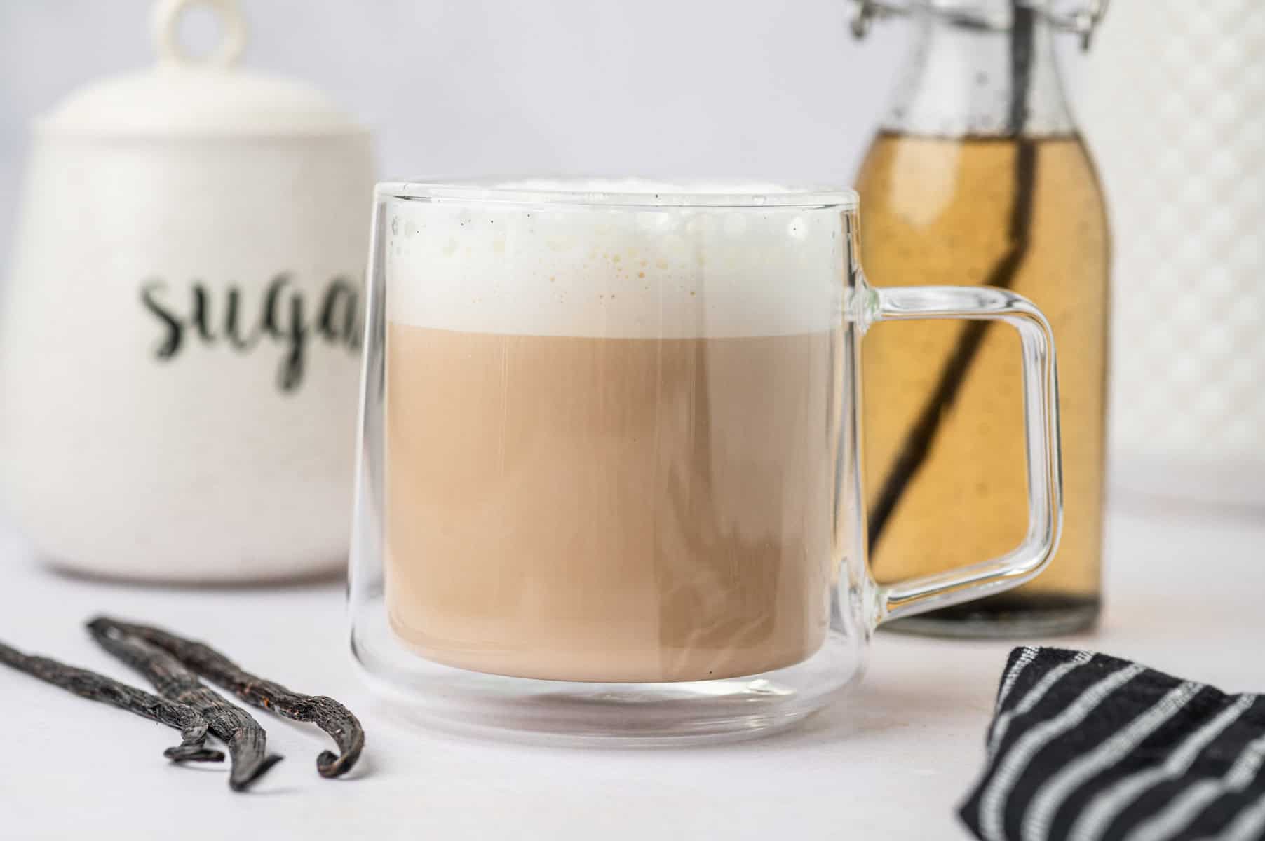 Horizontal image homemade vanilla bean latte in a clear glass mug.