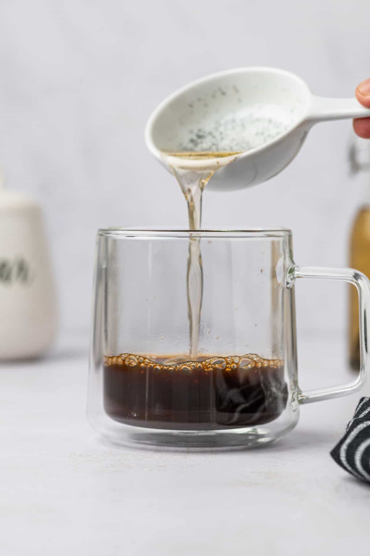 Homemade vanilla bean coffee syrup being added the vanilla bean latte recipe in a glass mug.