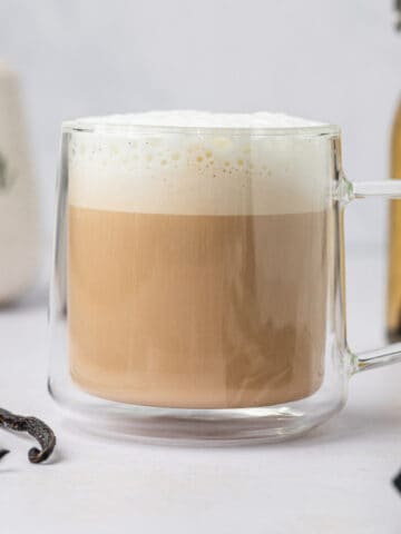 Homemade vanilla bean latte in a beautiful glass mug accompanied by vanilla beans on the side.