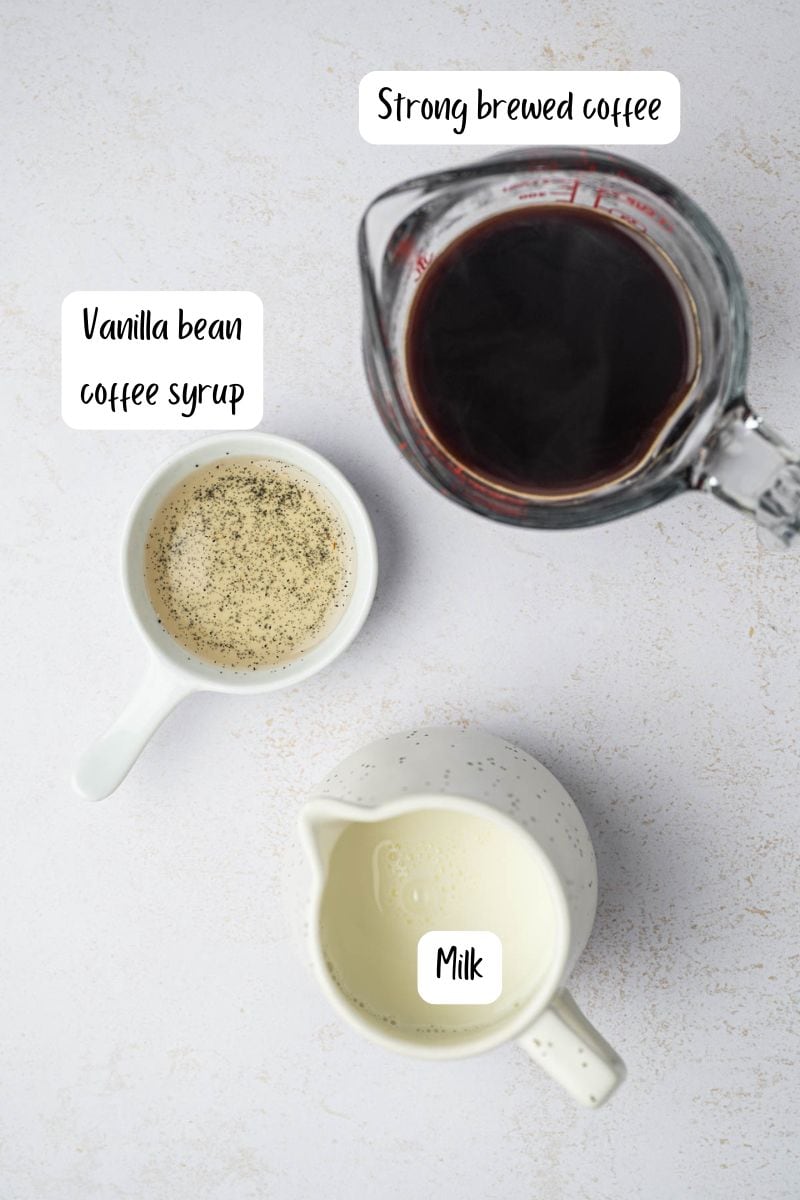 Ingredients laid out to make homemade best vanilla bean latte recipe on a marble countertop.