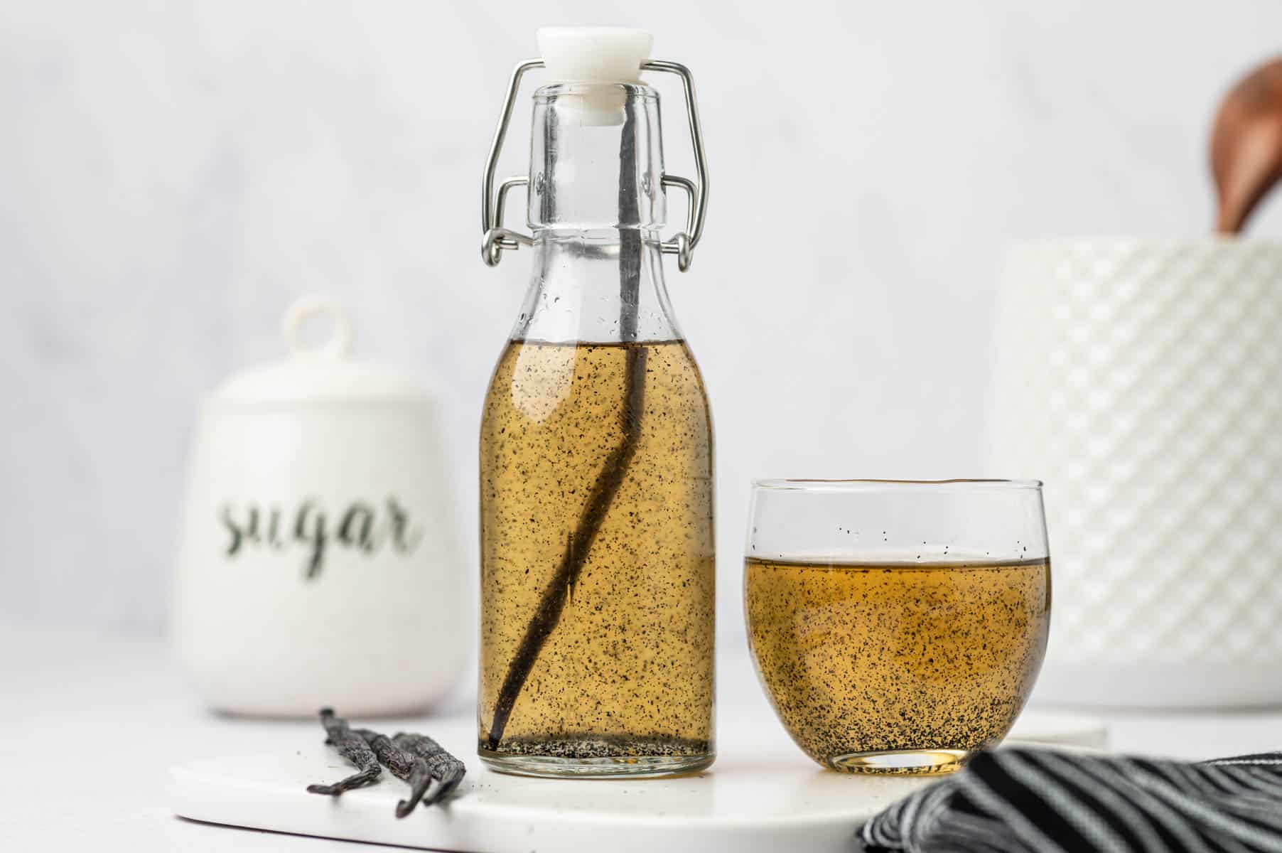 Vanilla bean syrup and vanilla coffee bean syrup placed in an airtight container and in a glass placed in a marble surface. 