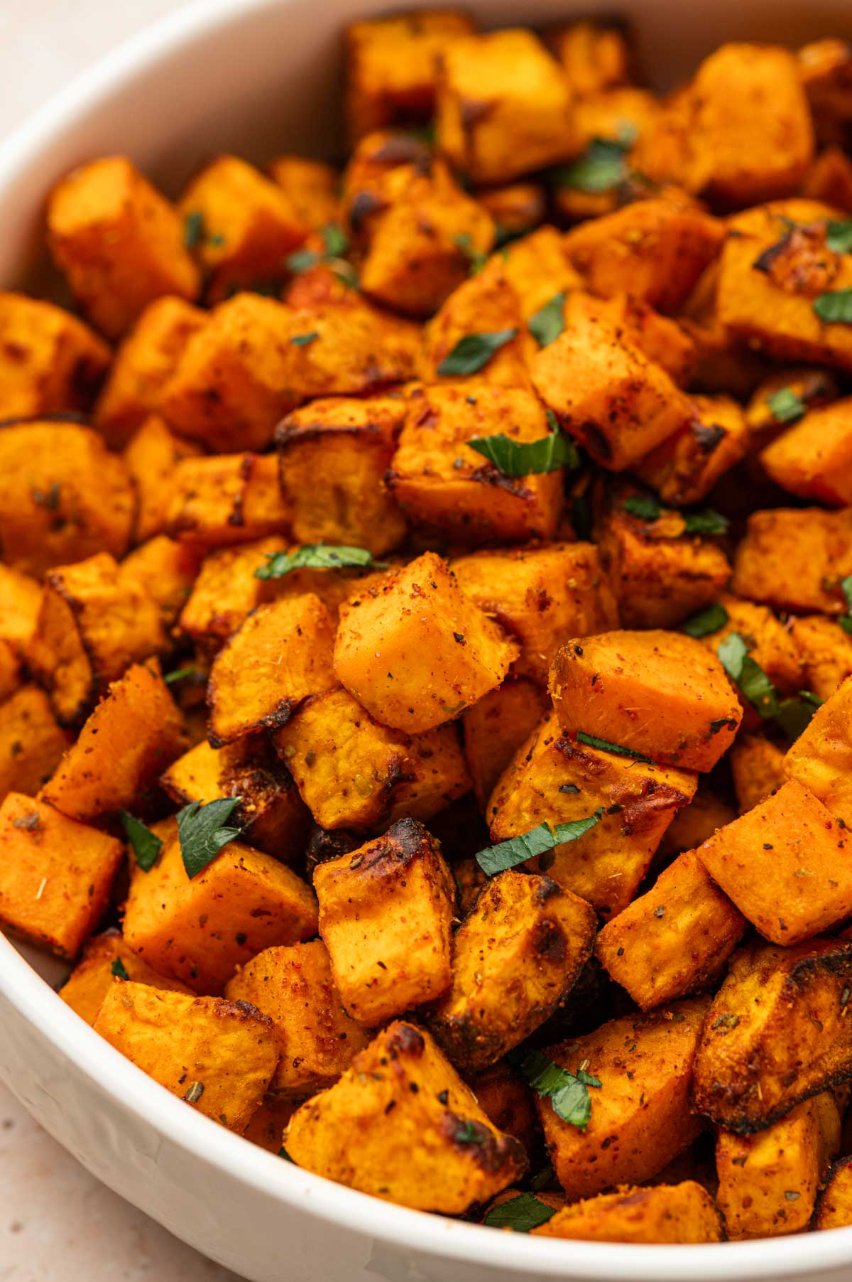 Close-up of seasoned sweet potato cubes in a white bowl, ready to serve.