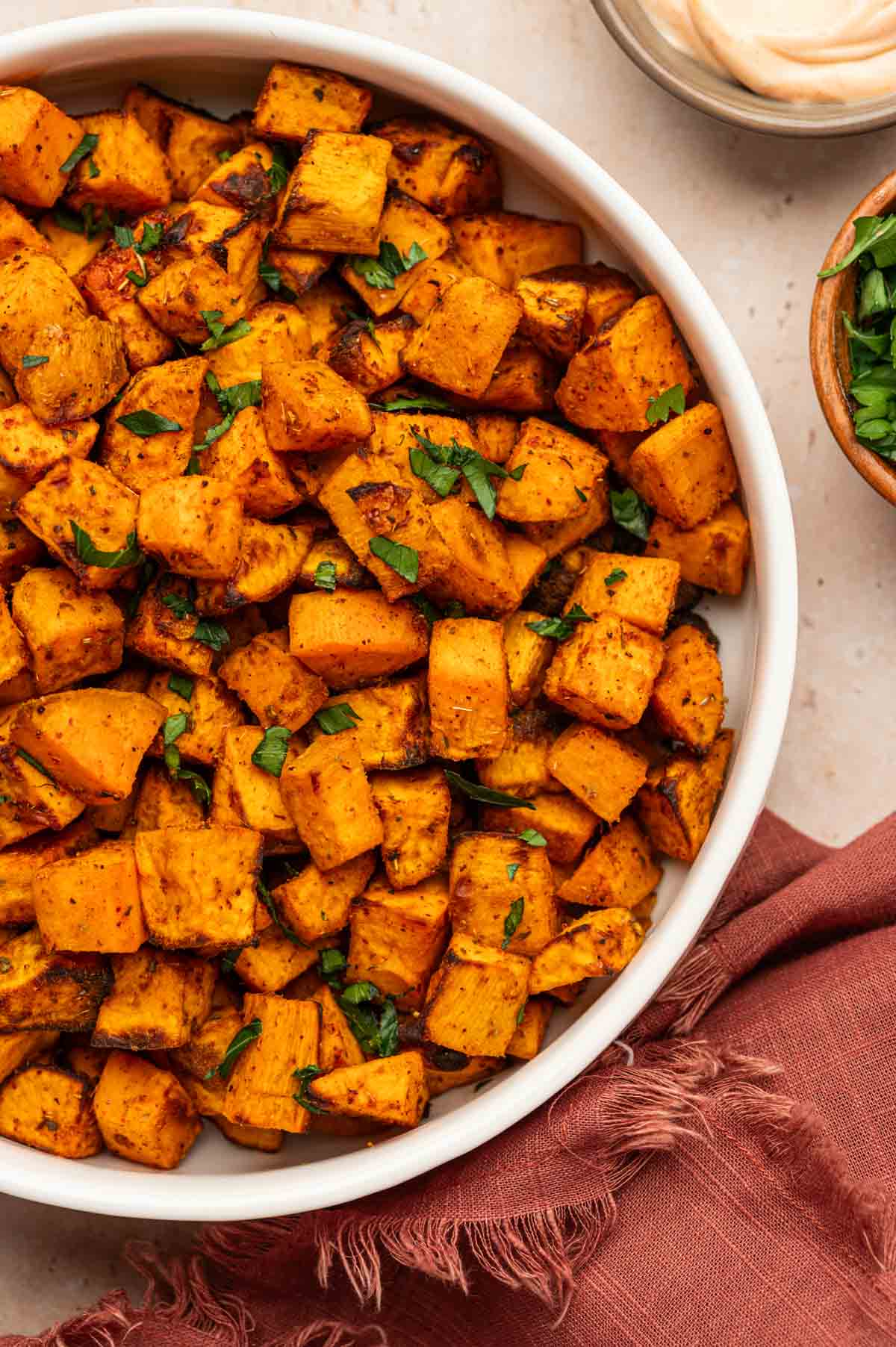 Golden, crispy sweet potato cubes with a sprinkle of fresh parsley on a white serving bowl.