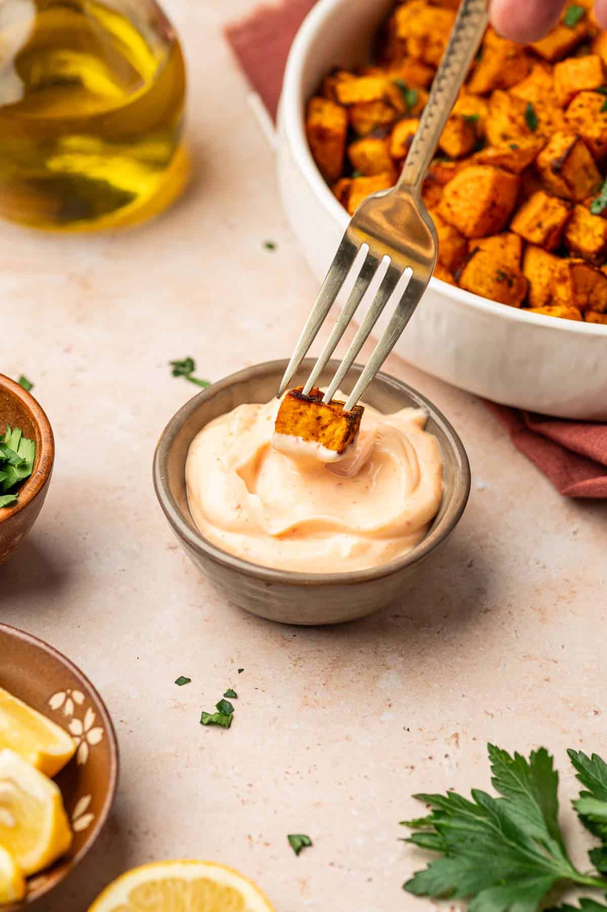 A bowl of crispy air-fried sweet potato cubes in the side and a fork with a piece of sweet potato cubes and dipping sauce.