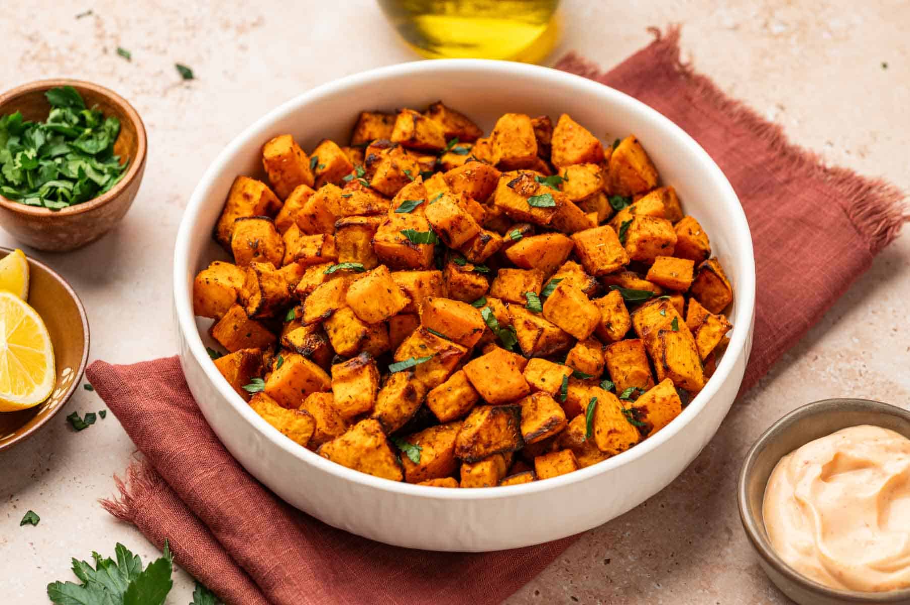 Air-fried sweet potato cubes on a white bowl with a side of dipping sauce.