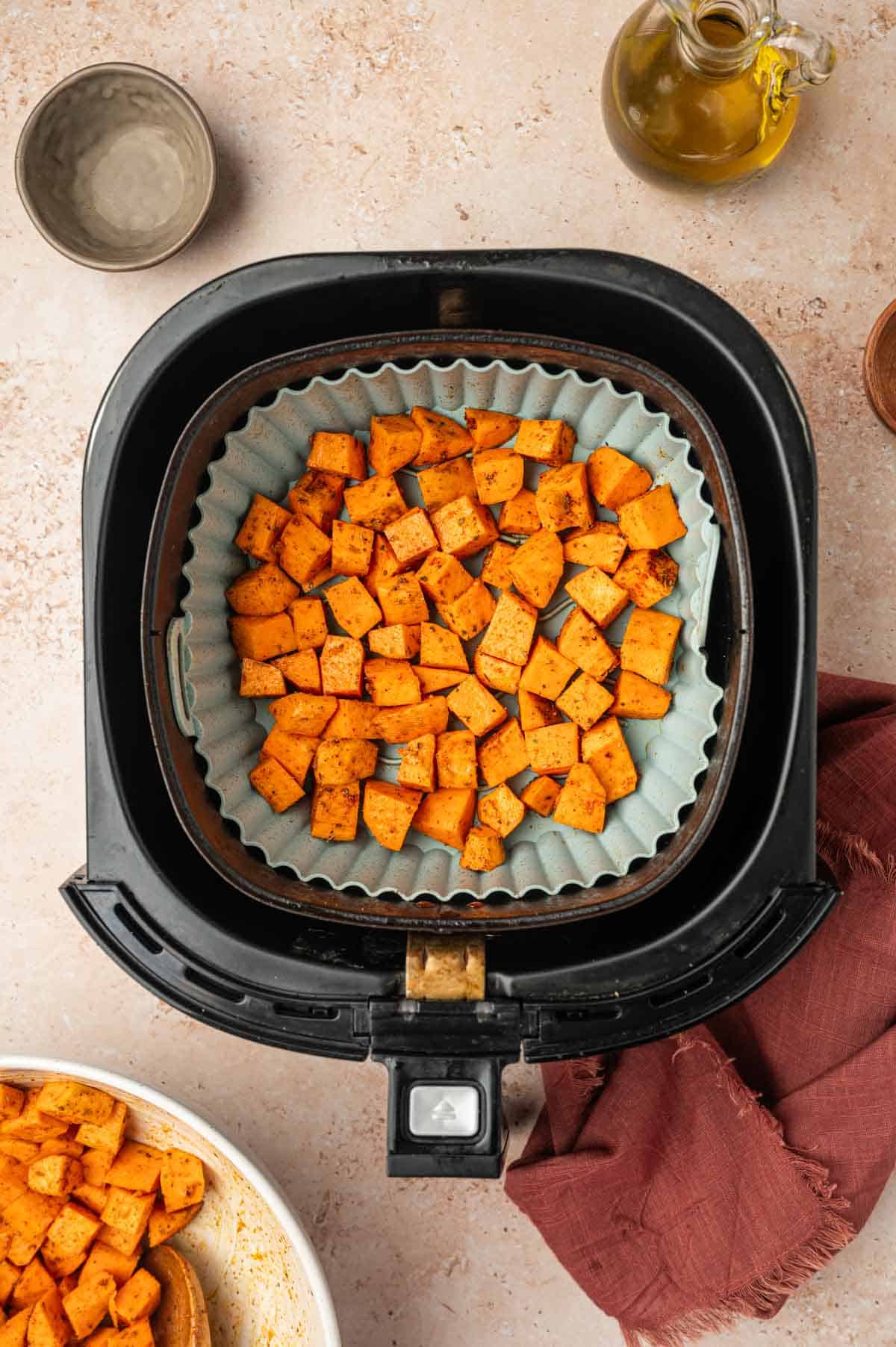 Well seasoned sweet potatoes cubes are in the slicon lined air fryer basket ready to air fry.