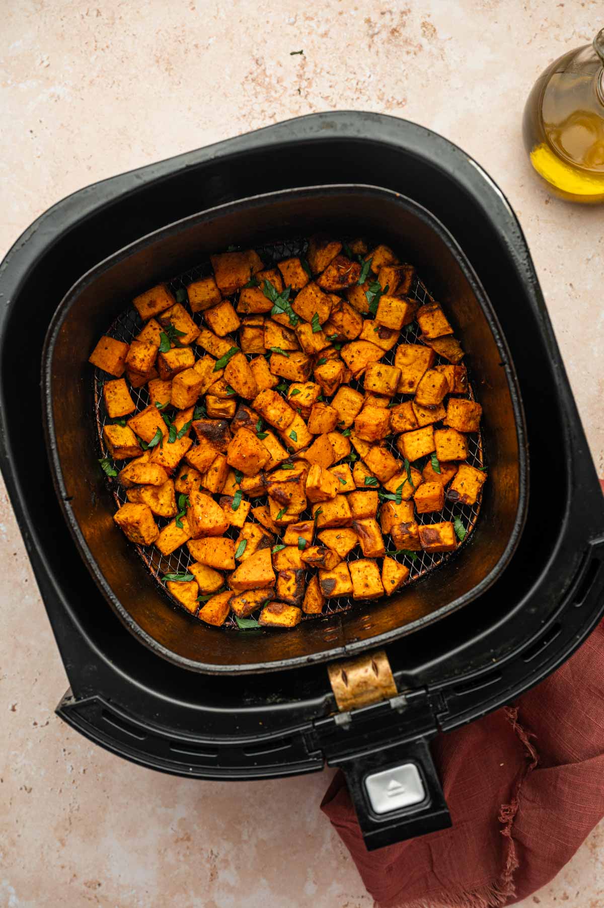 Air fryer sweet potato cubes with a sprinkle of fresh parsley in the air fryer basket.