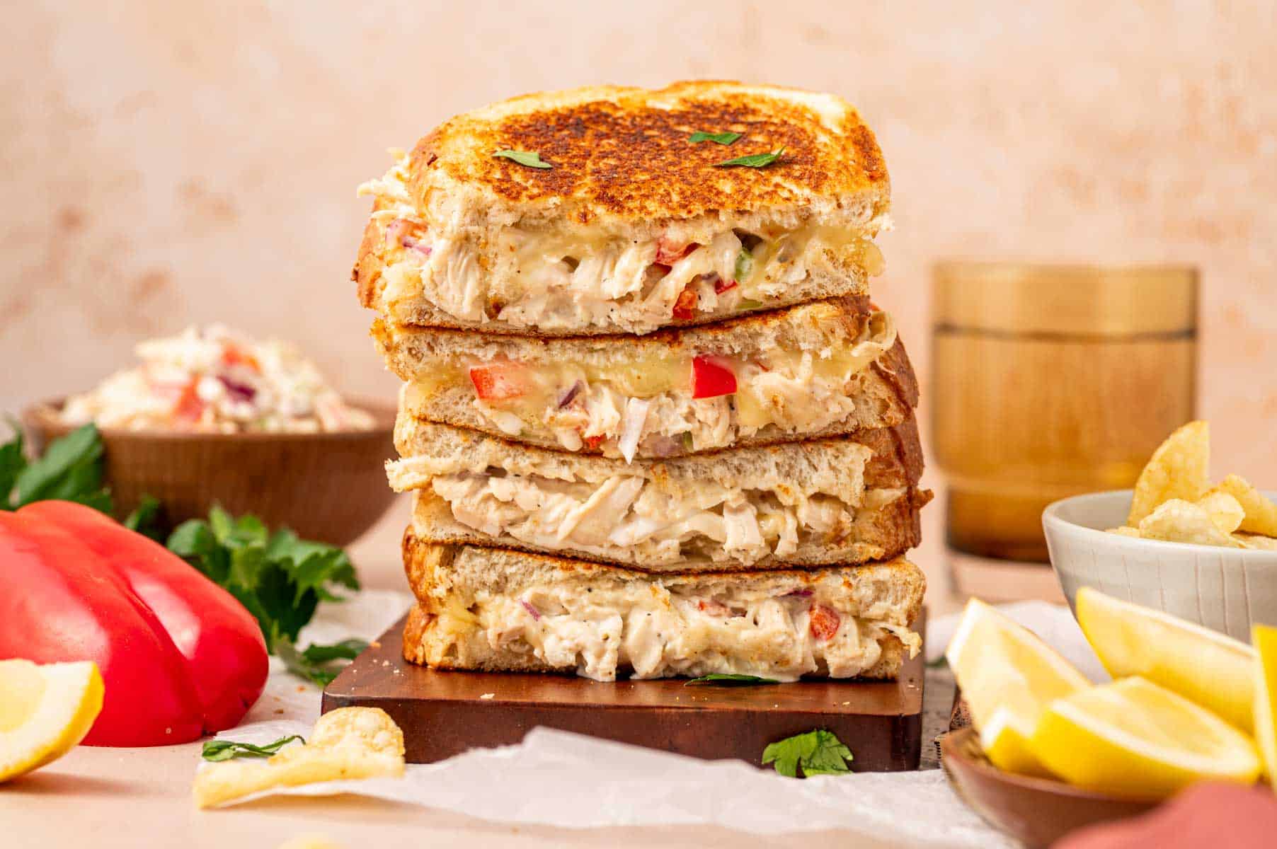 A chicken salad melt sandwich sliced in half, revealing its creamy filling, melted cheese, and toasted bread, served with coleslaw and chips.