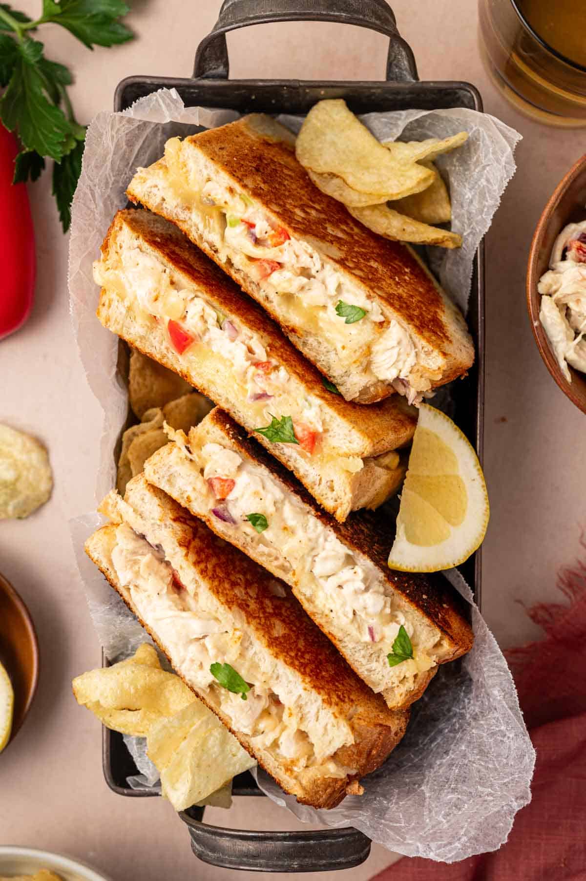 A perfectly grilled chicken salad melt sandwich on a rustic tray, with cheese oozing from the sides and garnished with fresh parsley.