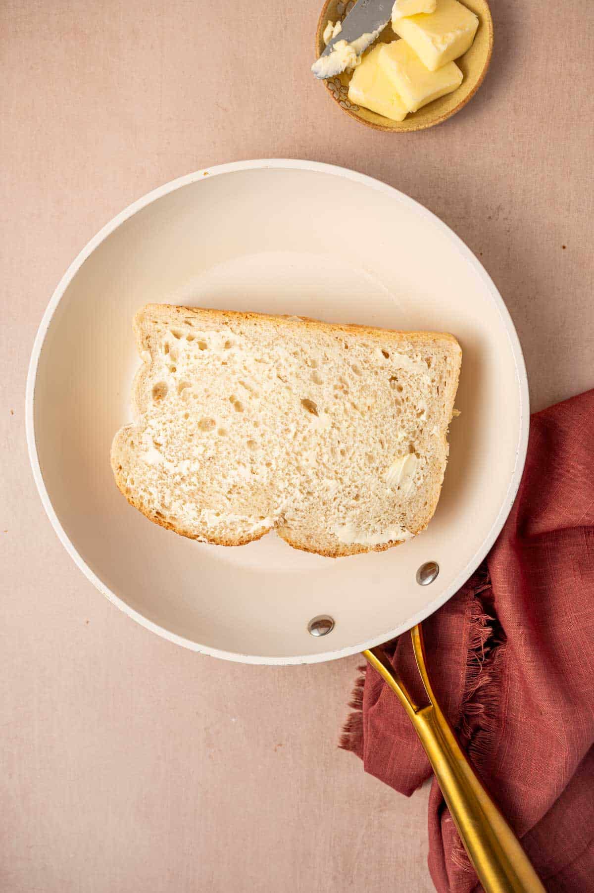 Butter being spread on top of the bread slice placed on a pan.
