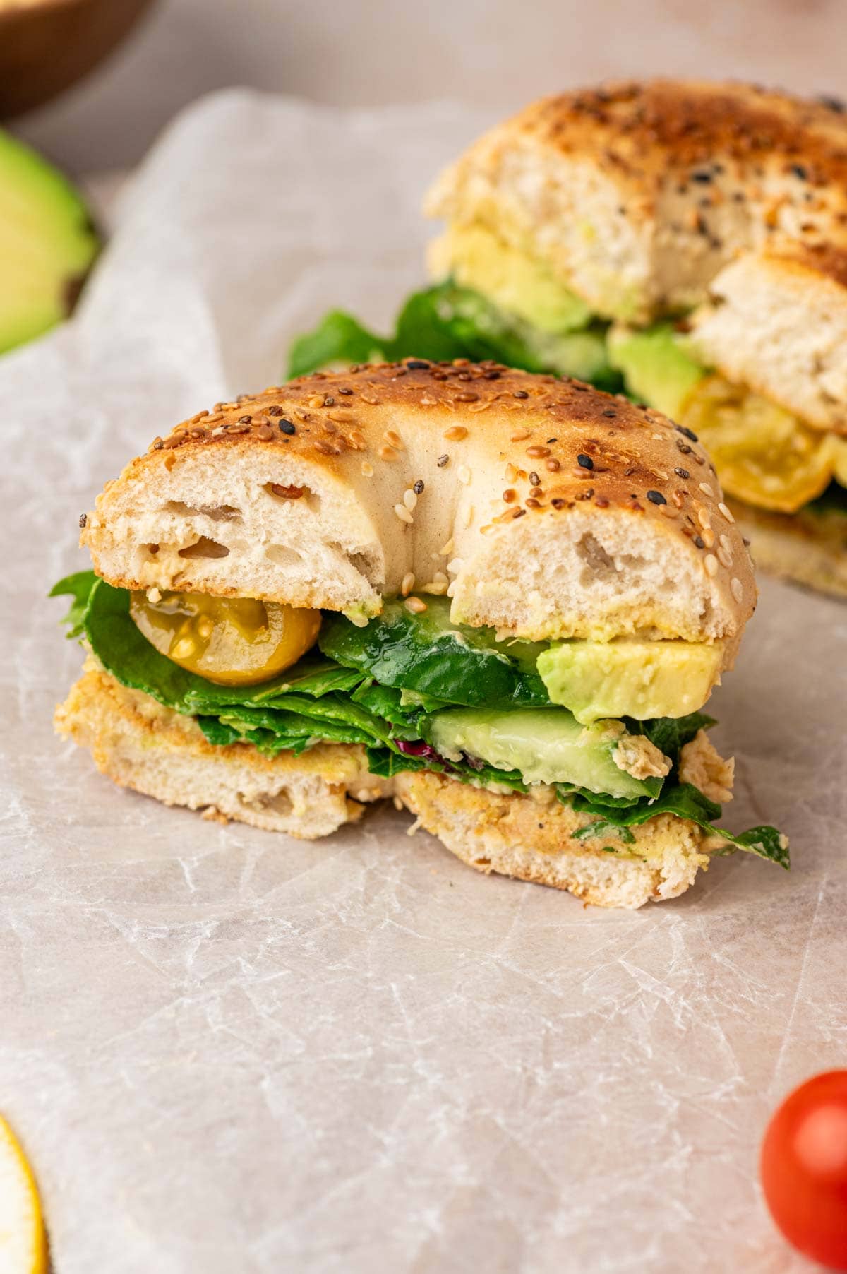 Close-up of a hummus bagel sandwich cut in half with creamy garlic-free hummus, colorful veggies, on a golden, crispy bagel.