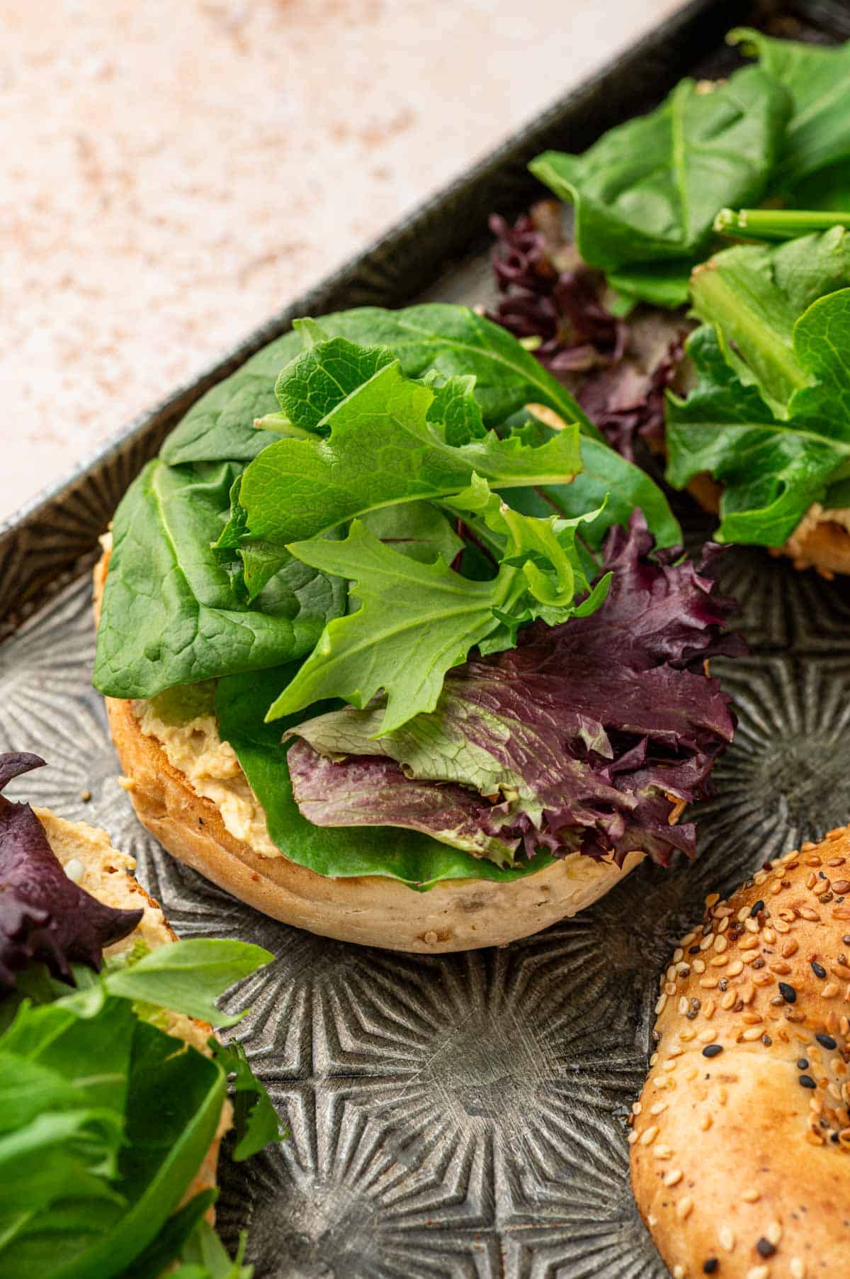Spring green mix placed above the hummus layer on the toasted bagel.