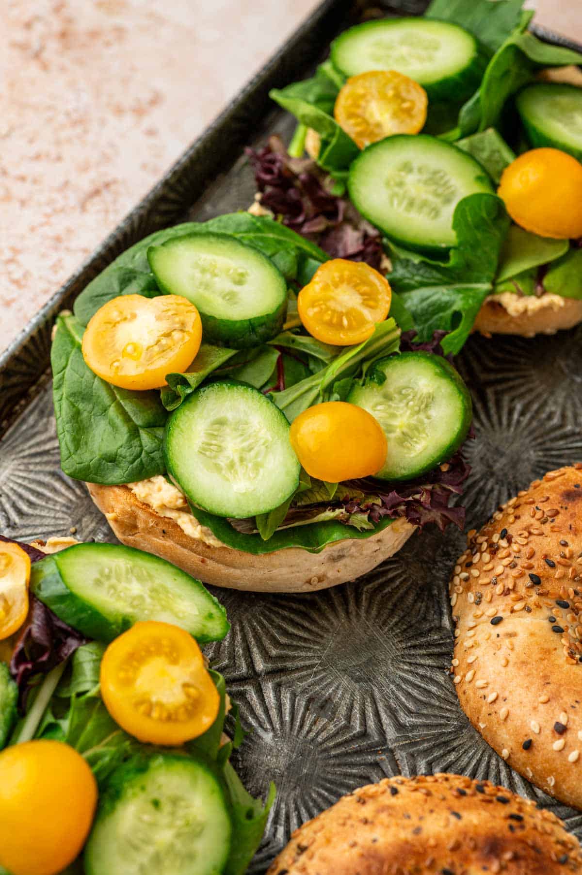 Cucumber slices and tomato slices placed on the bagels for hummus sandwich recipe.