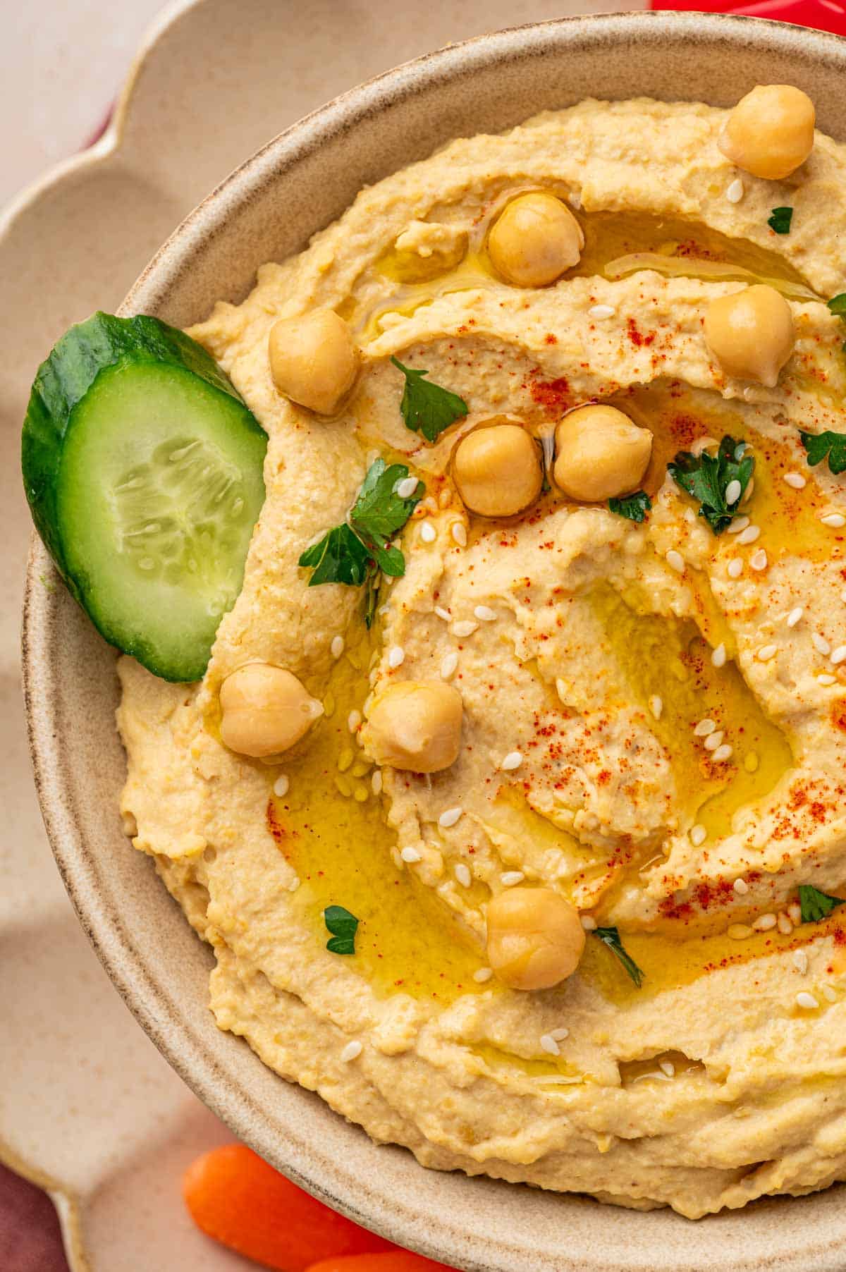 Cucumber slice being dipped in the creamy homemade hummus without garlic in a bowl.