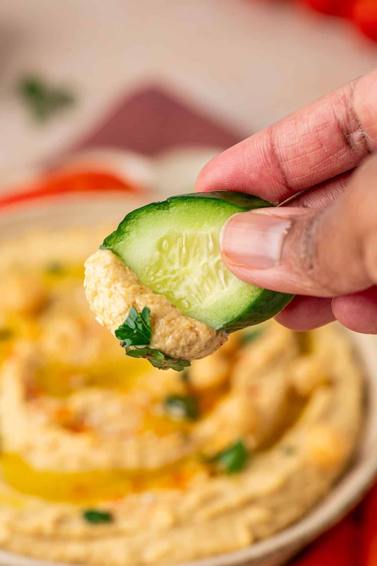 The cucumber slice being dipped in the creamy homemade humus.