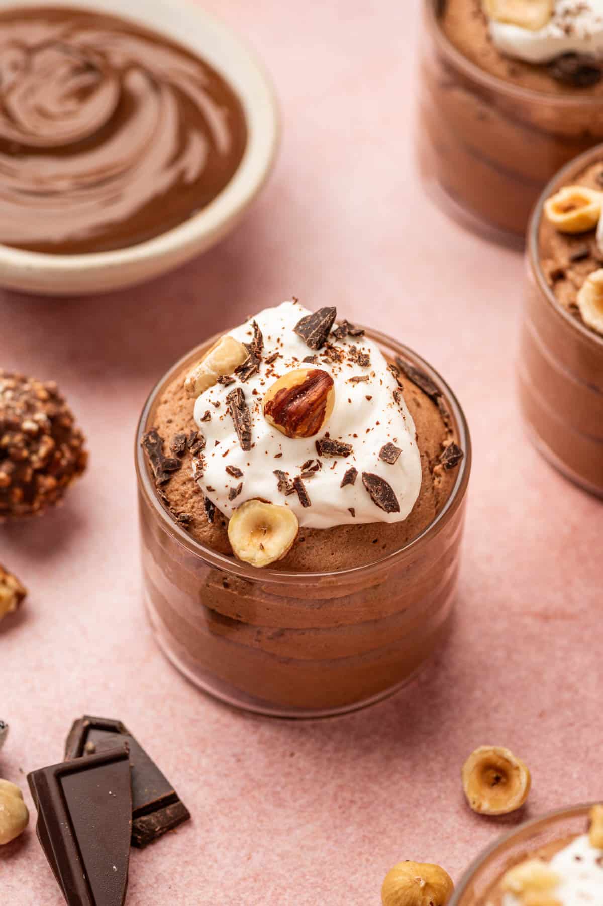 A glass cup filled with silky Nutella mousse, topped with whipped cream, chocolate shavings, and chopped hazelnuts.