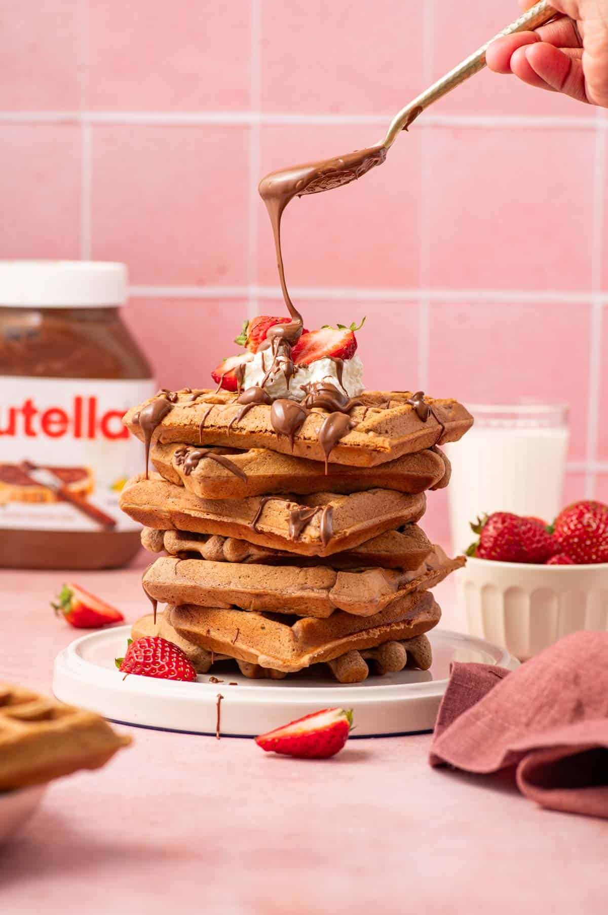 A stack of warm Nutella waffles served topped with whipped cream, fresh strawberries, and a rich chocolate-hazelnut drizzle, creating a decadent and mouthwatering brunch treat.
