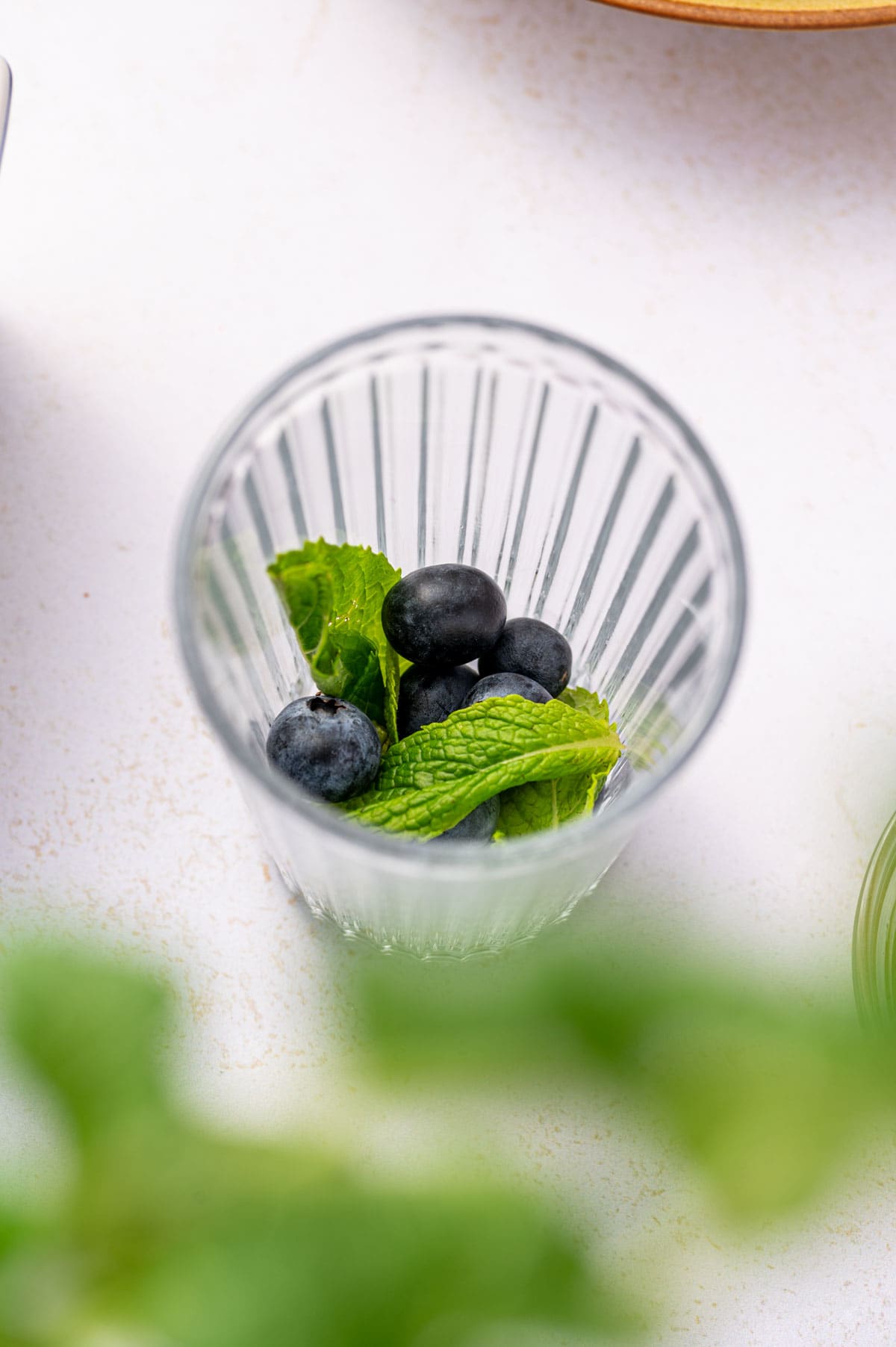 Blueberries, mint, simple syrup, lime juice being added to make blueberry mojito mocktail.