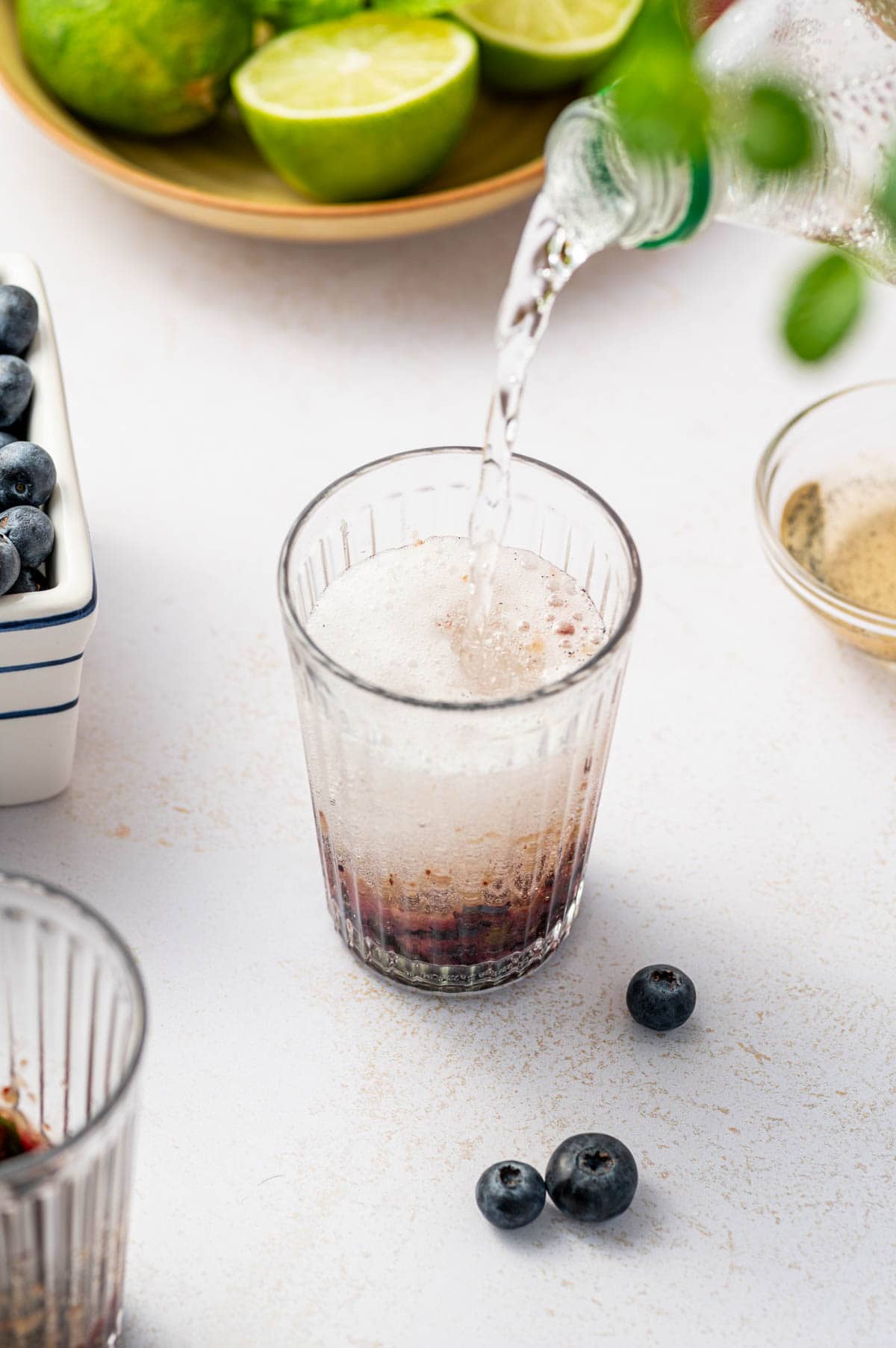 Soda being poured over the glass for making virgin blueberry mocktail.