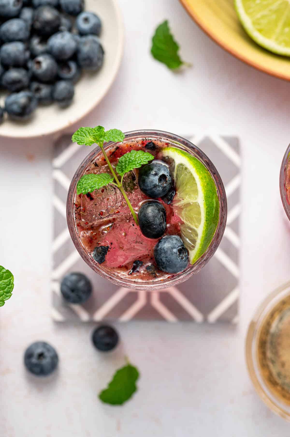 Close-up of blueberry mojito mocktail garnished with mint leaves and lime slices.