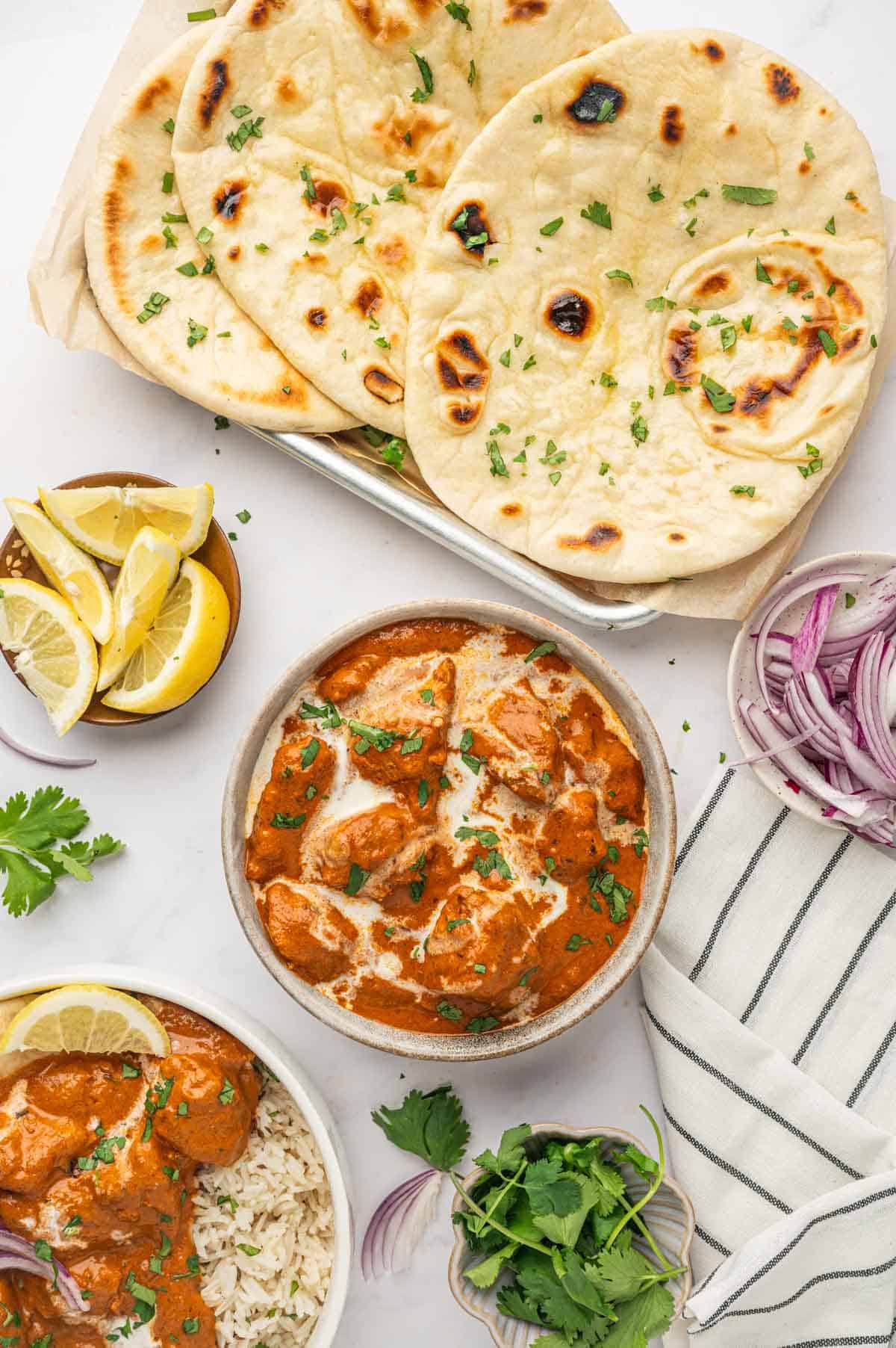 Flatlay of homemade butter chicken with naan, rice, and Indian-style.