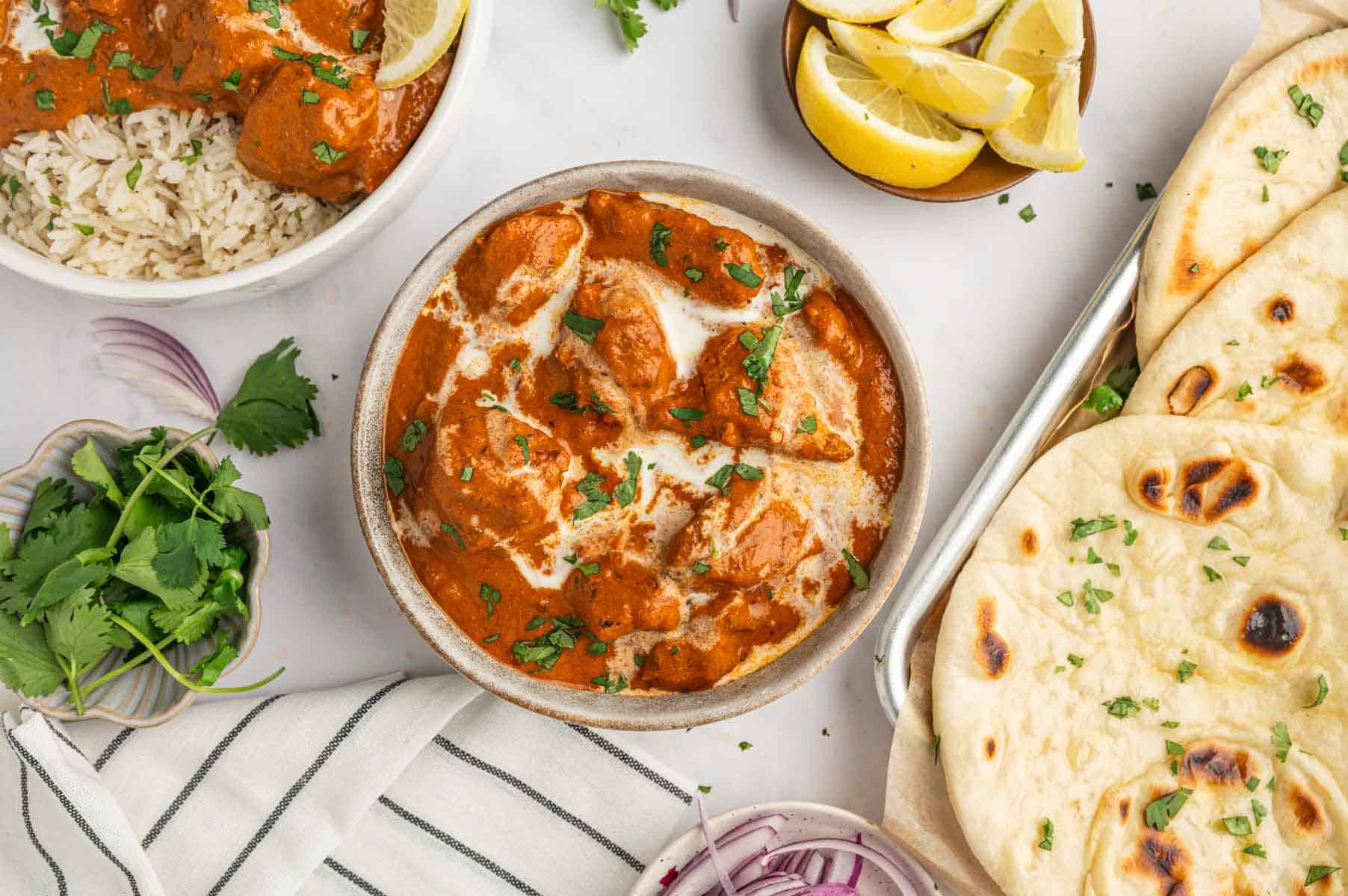 Homemade butter chicken in rich tomato sauce with a stack of warm butter naan in the side.