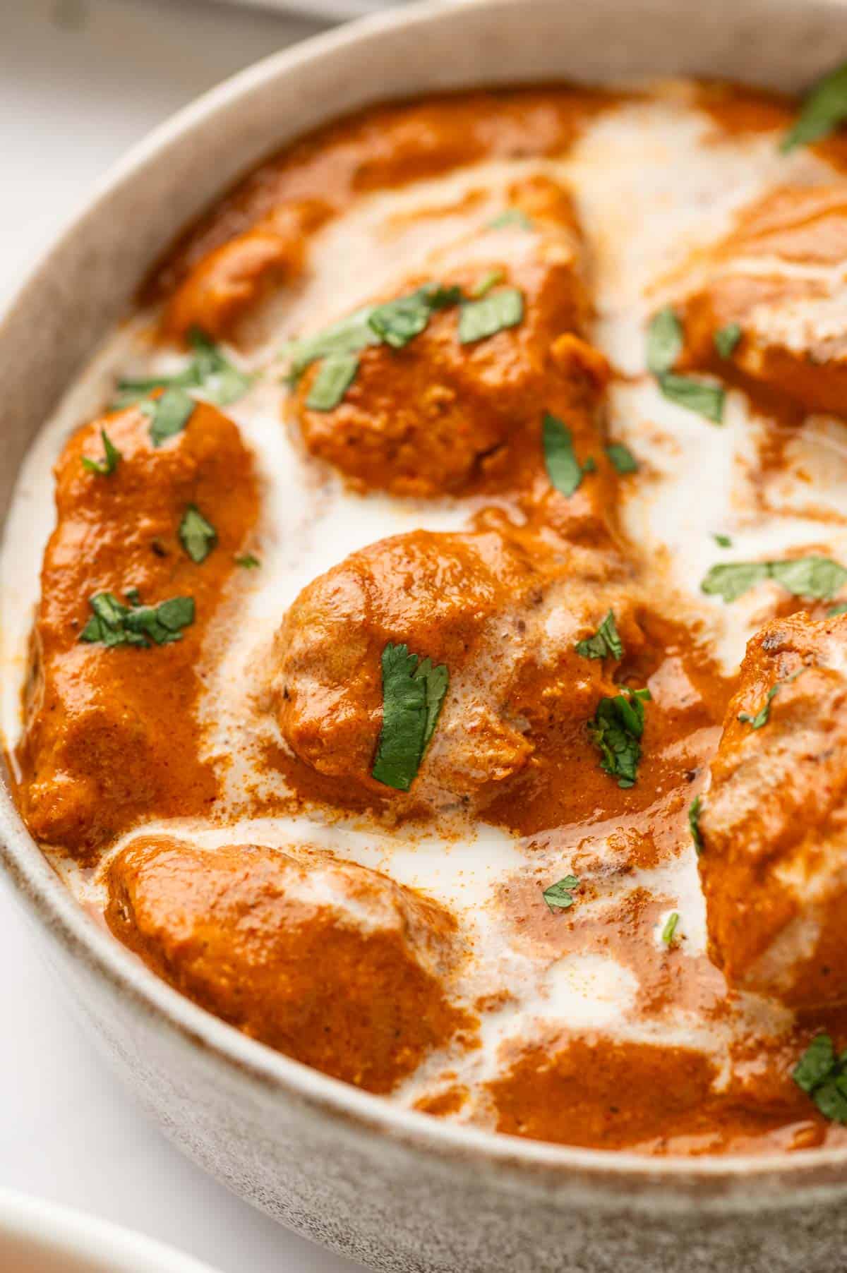 Creamy butter chicken close up shot. Garnished with heavy cream and cilantro.