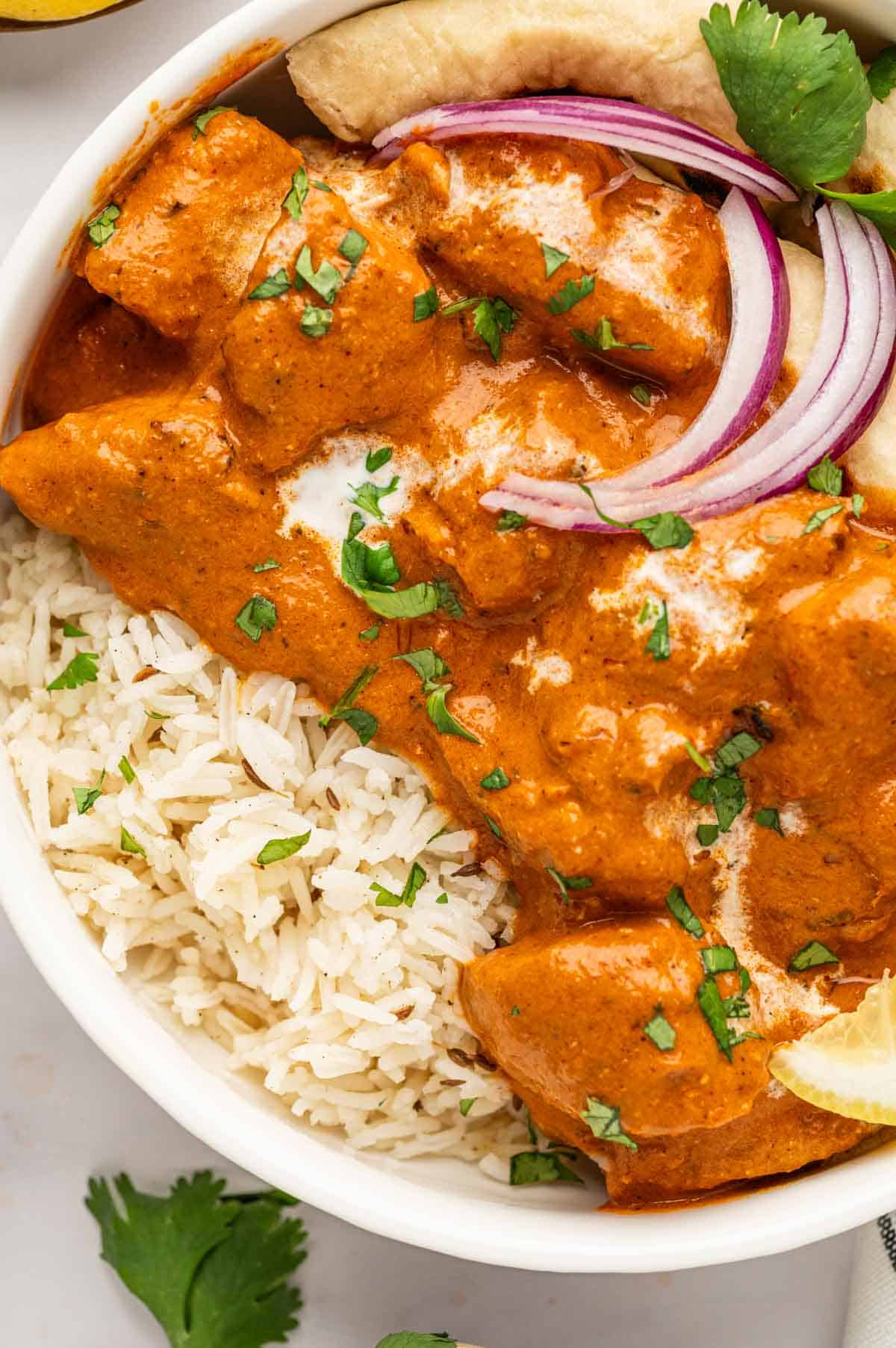 Close up shot of Indian butter chicken and naan served with pickled onions and raita.