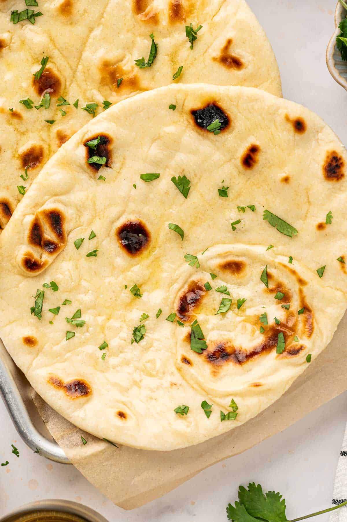 Close-up of butter naan bread brushed with melted butter and garnished with cilantro.