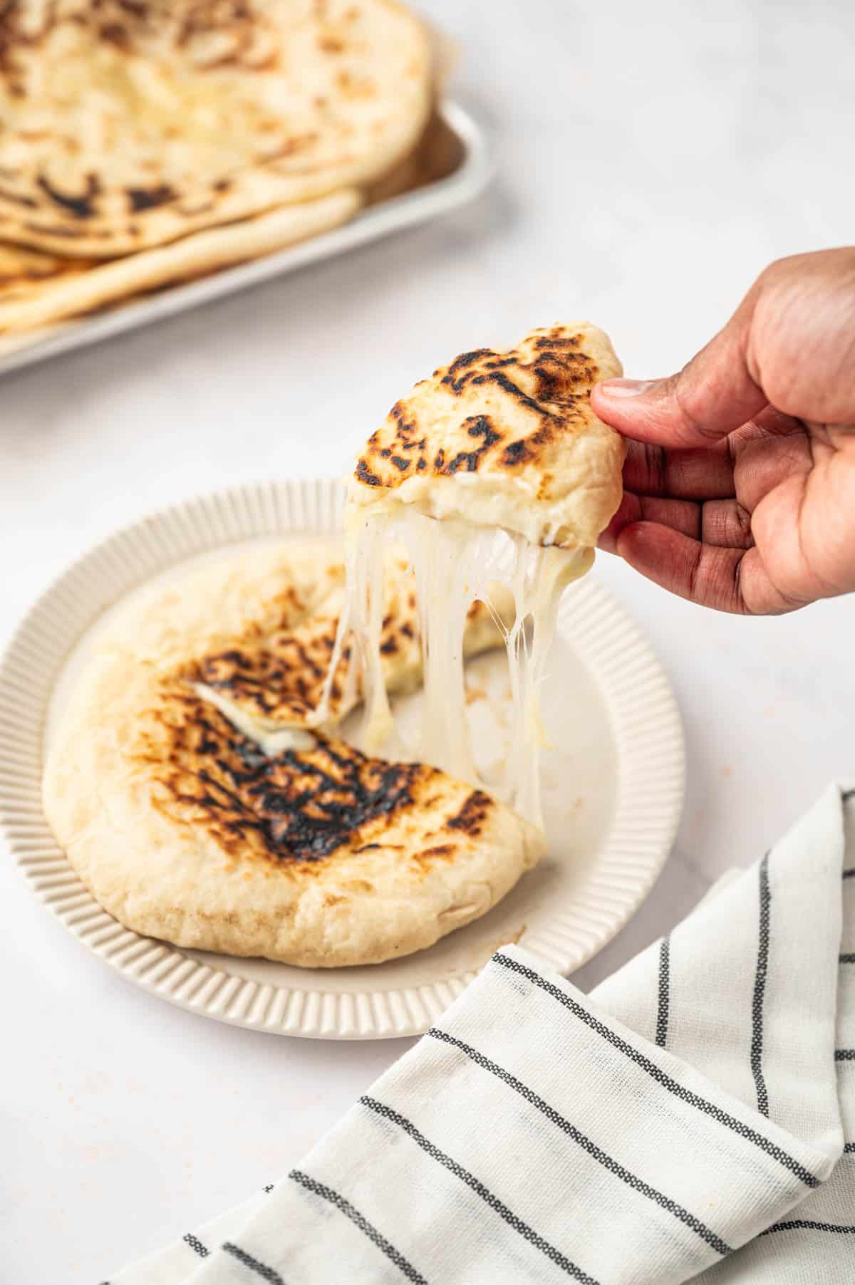A hand taking a piece of cheese naan and the cheese is streching over.