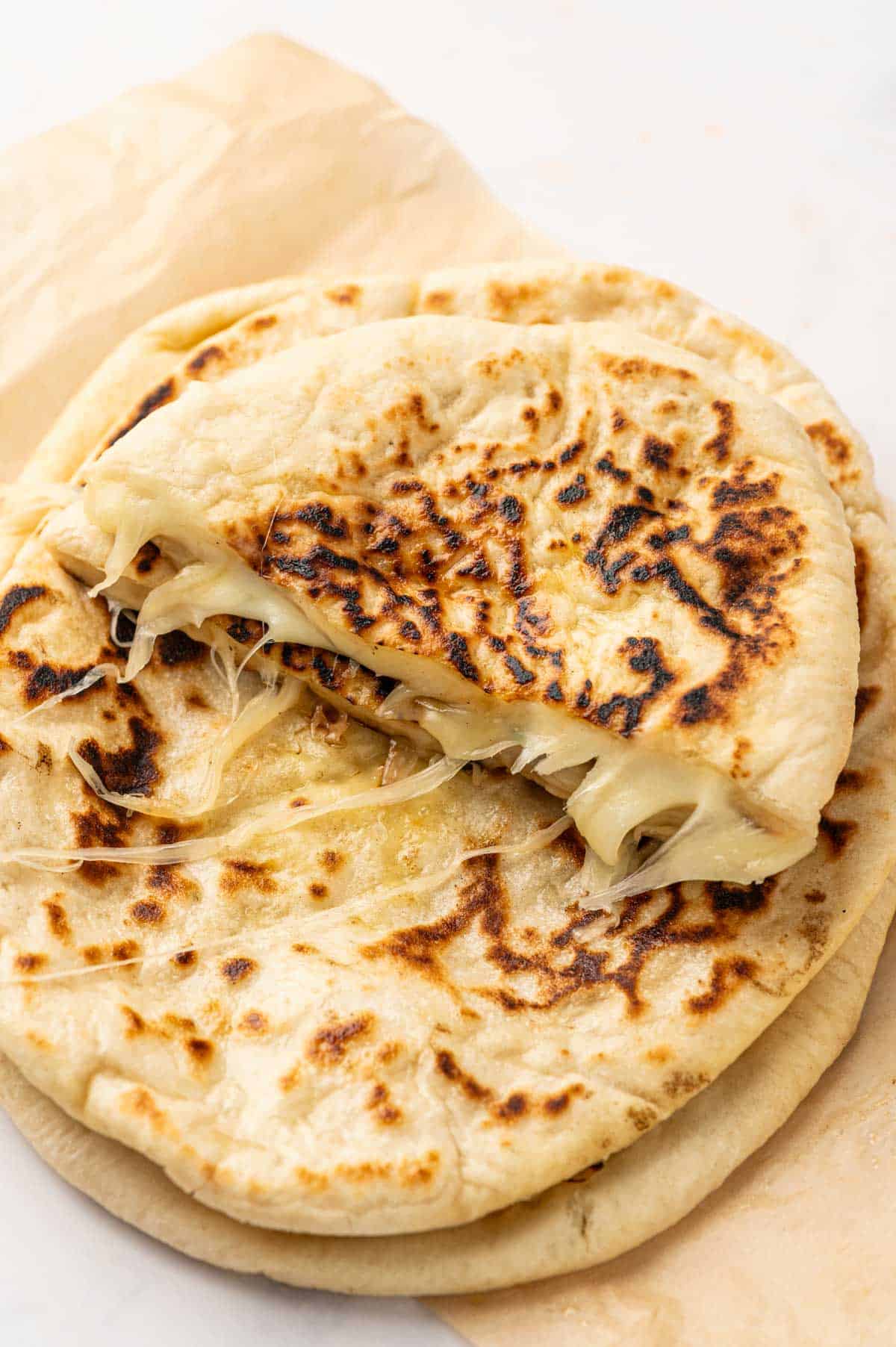 Cheese-stuffed naan bread stacked on a baking paper with melted cheese oozing out.