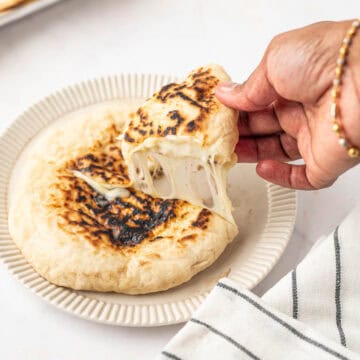 A hand is taking a slice of cheese naan and the cheese is melting and stretching.