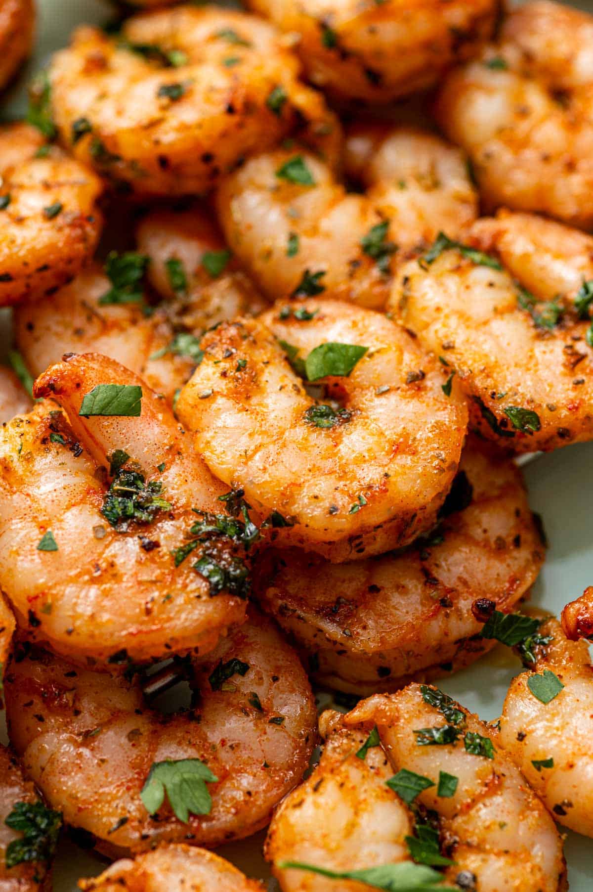 Close-up of oven-baked shrimp skewers arranged on a platter, garnished with fresh parsley and lemon wedges.