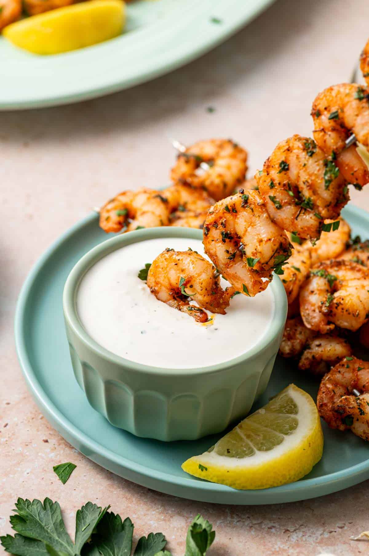 Skewered shrimp seasoned with herbs and spices, baked to perfection being dipped into the parmesan ranch dip sauce.