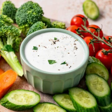 Parmesan ranch dip in a green bowl surrounded by veggies like broccoli, carrots, cherry tomatoes and cucumber.