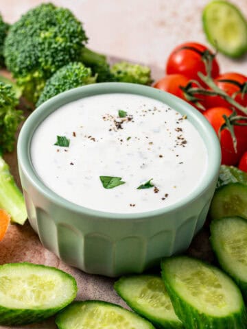 Parmesan ranch dip in a green bowl surrounded by veggies like broccoli, carrots, cherry tomatoes and cucumber.