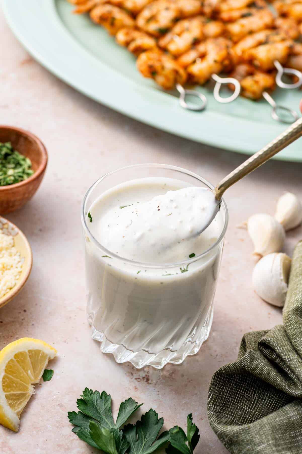 A spoon is taking a spoonful of parmesan ranch dressing dipping sauce.