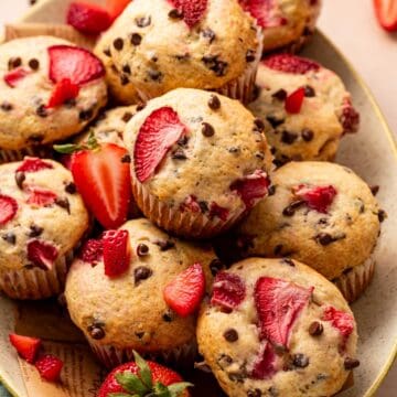 Stack of strawberry muffins with chocolate chips and fresh strawberries on the side.