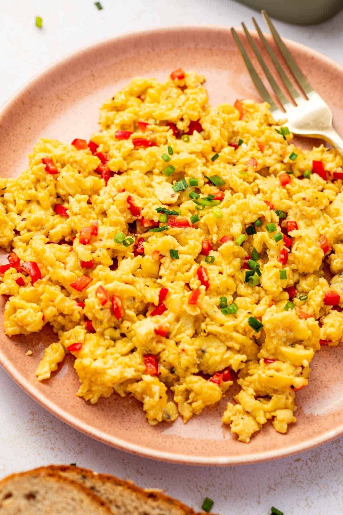 Soft and fluffy chili scrambled eggs served in a pink plate with chives on top. With fork on the side.
