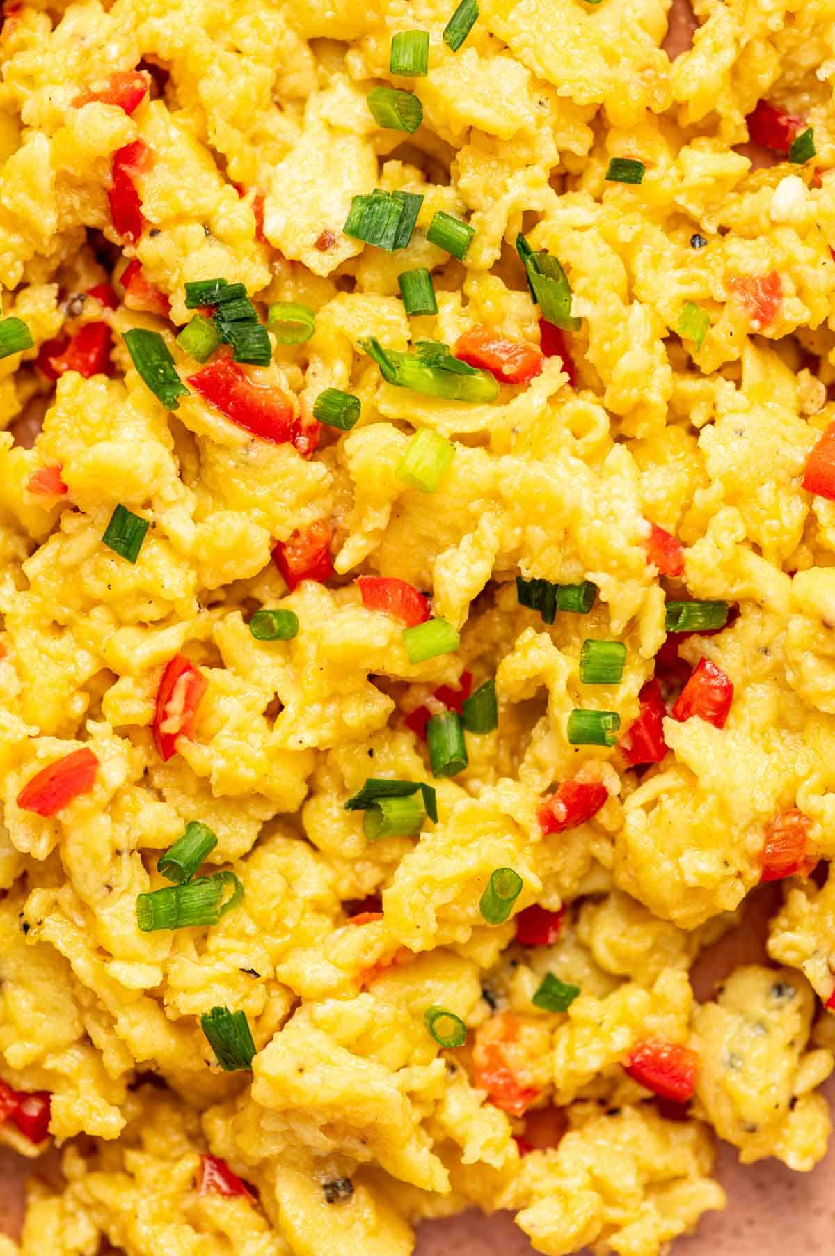 Close-up of silky scrambled eggs with red chili pepper slices and fresh herbs.