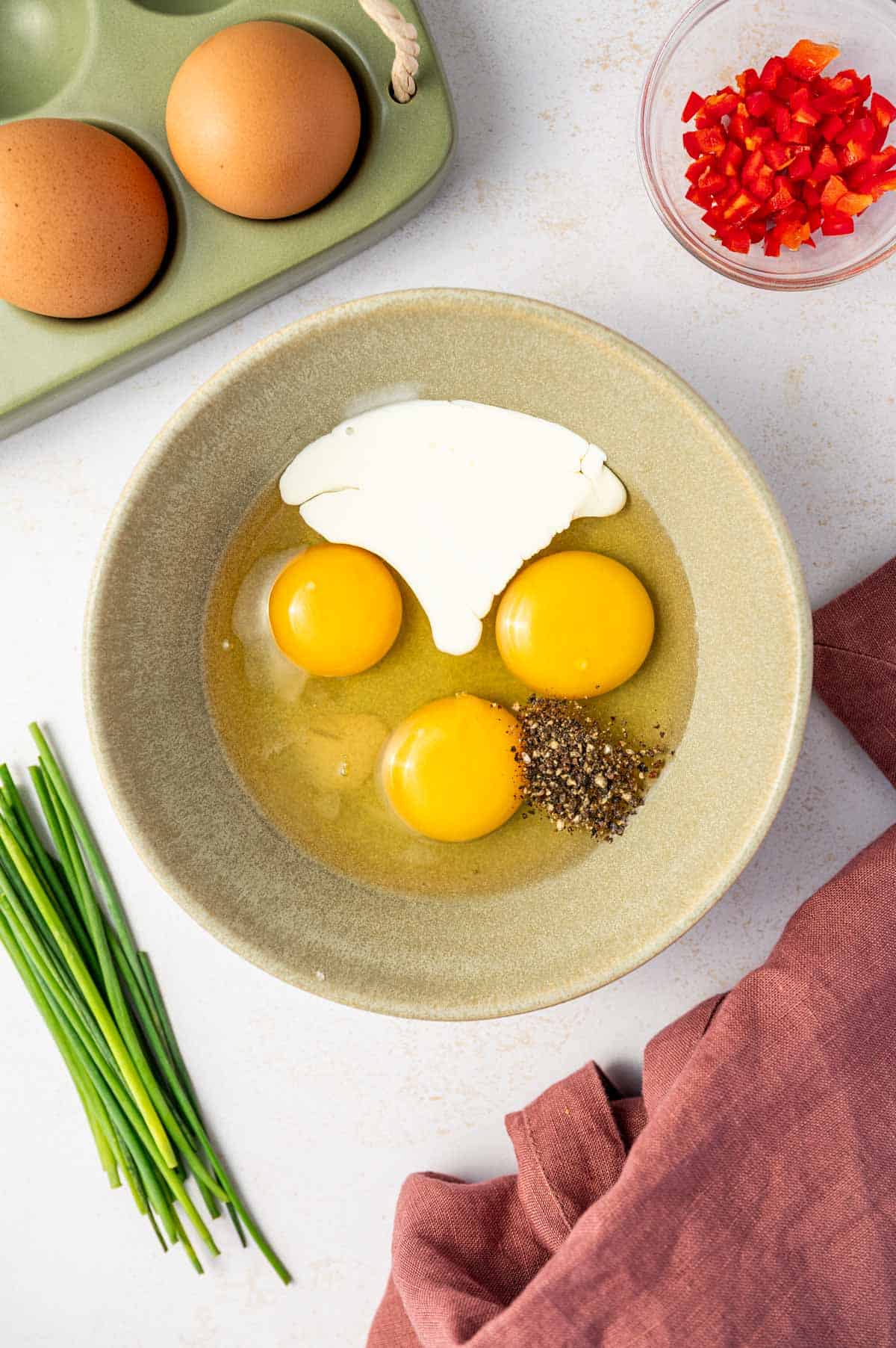 Ingredients being added in a green bowl to make creamy scarmbled egg with chili.