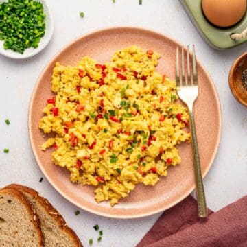 Overhead view of creamy scrambled eggs with red chili and chives garnish.