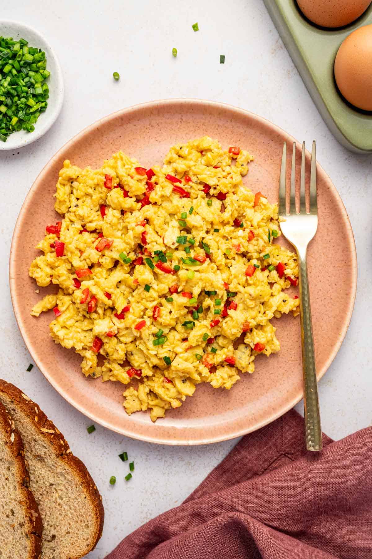Creamy scrambled eggs with chili served on pink plate, sprinkled with fresh chives.