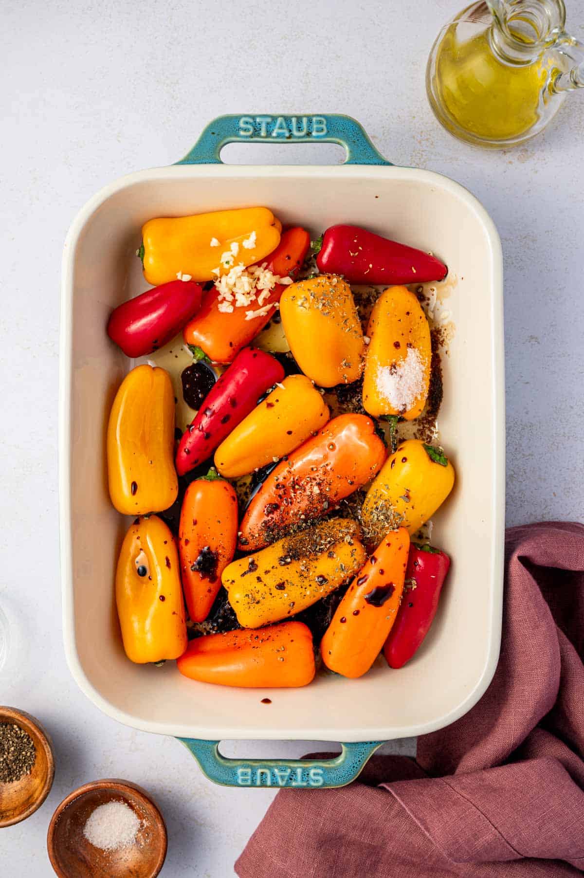 Mini peppers are arranged in a baking dish and seasoned.