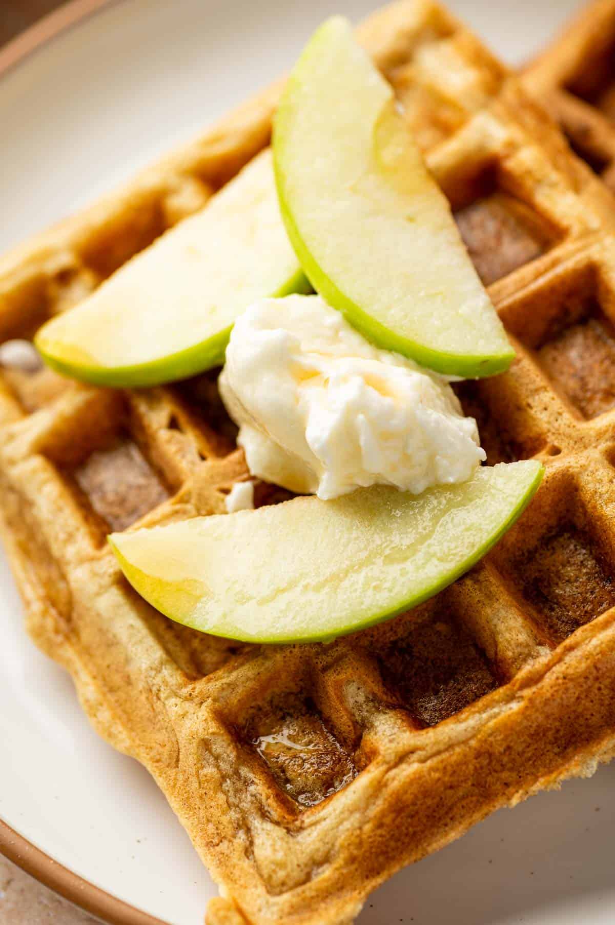 Warm cinnamon apple waffles served with whipped cream and sliced apples